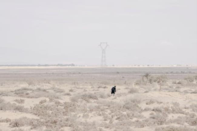 A figure, fully clothed, walking through the Tunisian desert